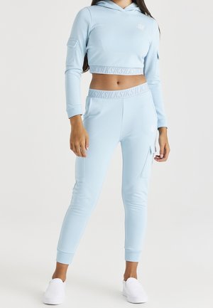 Sweat à capuche court bleu clair à manches longues avec une poche avant, assorti à un pantalon de jogging avec poches latérales et poignets ajustés.