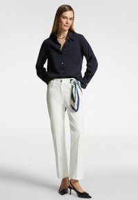 Camicia navy con bottoni, pantaloni bianchi con una sciarpa legata in vita e tacchi neri a punta. Tessuto morbido e vestibilità su misura.