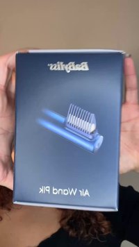 Skjeggtrimmeremballasje i marineblått, med en kam og en apparatgrafikk. Teksten sier "Beard Wands" øverst og "Air Wand Pick" under.