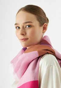 Grande écharpe multicolore avec des tons de rose et de marron dans un design à blocs, fabriquée dans un matériau doux, drapée autour du cou.