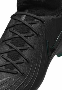 Primo piano di una scarpa sportiva nera con texture, con dettagli nei lacci e un logo Nike in gloss sulla parte laterale.