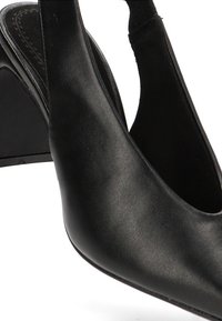 Zapato de tacón alto negro tipo slingback, fabricado en cuero suave, con un tacón triangular y diseño abierto en la parte delantera.