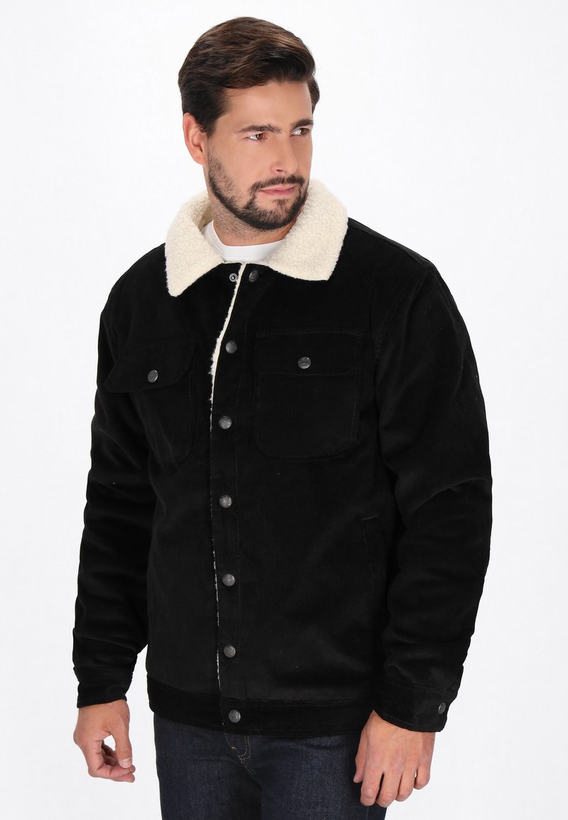 Fekete kordbársony dzseki krém színű műshearling gallérral. Két mellzseb és fémből készült gombok jellemzik. Texturált anyag, amely strukturált szabással rendelkezik.