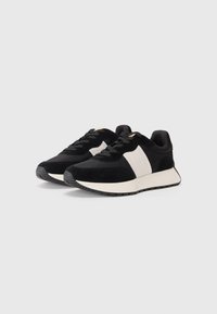 Črne in bele športne superge z nubukom in tekstilnim zgornjim delom, s popolno belo črto in teksturiranim gumijastim podplatom za boljši oprijem.