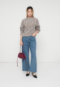 Gebreide trui van meerkleurig garen, hoge hals, lange mouwen; gecombineerd met lichtblauwe wijde jeans, zwarte puntige ballerina's en een bordeauxrode handtas.