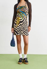 Dress with a beige and black geometric pattern, featuring multicolored leaf motifs. Paired with a blue textured bag and black sneakers.