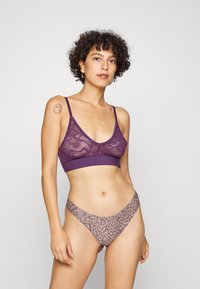 Sutiã de renda roxa com alças ajustáveis e uma faixa lisa. Combinado com cuecas de corte baixo estampadas com padrão de leopardo em um tom castanho claro.