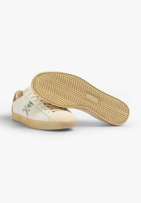 White leather sneakers with beige accents and suede detail, featuring a textured rubber sole and a zigzag pattern on the bottom.