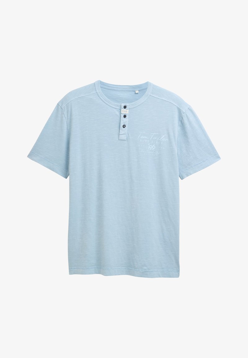 Camiseta de manga corta azul claro con cuello redondo, tapeta de botones en la parte delantera y un diseño impreso sutil en el pecho. Textura suave.