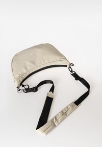 Beige gepolsterte Schultertasche mit abgerundetem Oberteil, schwarzem Reißverschluss und verstellbarem schwarzen Tragegurt. Glatte Textur mit Nylonmaterial-Akzenten.