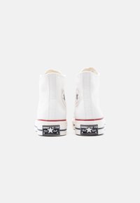 Αθλητικά παπούτσια υψηλού πάνω λευκού καμβά με στρογγυλή λογότυπη επιγραφή, κόκκινη λωρίδα διακόσμησης και μαύρη ελαστική σόλα με λευκές και μπλε λεπτομέρειες.