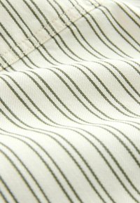Gros plan sur un tissu beige avec de fines rayures verticales noires et des coutures visibles le long d'une couture.