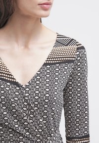 Black and cream patterned wrap dress with a deep V-neck, featuring geometric and diamond designs, long sleeves, and a textured fabric.