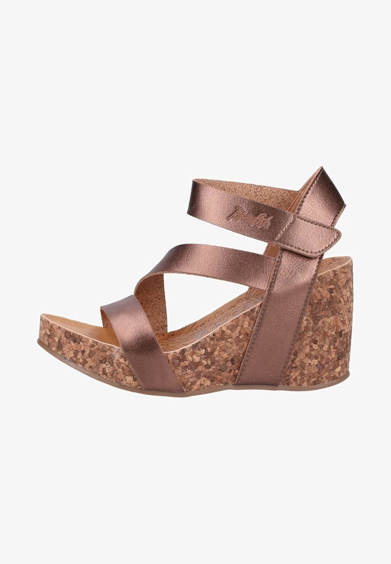 Sandały na korkowej koturnie z bronzowymi metalicznymi paskami. Posiadają krzyżujące się paski i teksturowaną bazę korkową. Gładkie, błyszczące wykończenie pasków.