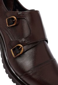 Donkerbruine leren monk strap schoenen met twee verouderde messing gespen en uitgebreide stiksels op een geribbelde zwarte zool.