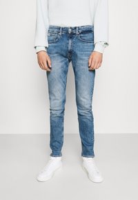 Ljust blå jeans med slim fit och blekt mönster, med fem fickor och knappstängning, ihop med vita sneakers.