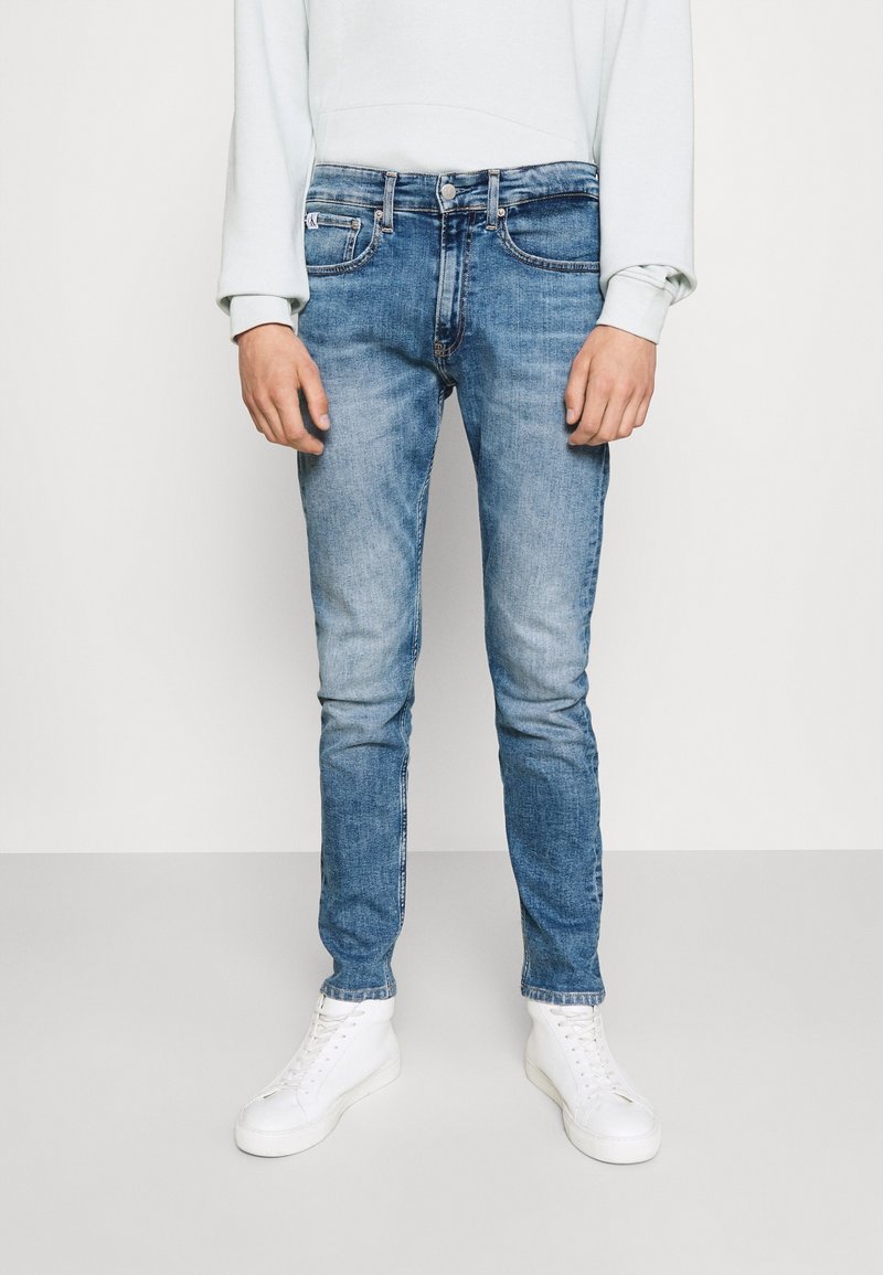 Ljust blå jeans med slim fit och blekt mönster, med fem fickor och knappstängning, ihop med vita sneakers.