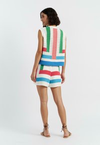 Ensemble en crochet comprenant un gilet et un short blancs, ornés de rayures multicolores horizontales et verticales en vert, bleu, rose et rouge.