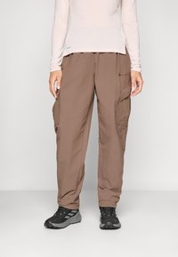 Brown cargo pants with multiple side pockets, made from lightweight fabric. Paired with a light long-sleeve shirt and black sneakers.