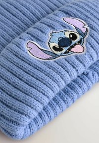 Lichtblauwe gebreide beanie met ribbelstructuur en een geborduurd Stitch-personage aan de voorkant, met zwarte, witte en paarse accenten.