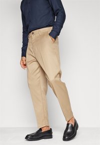 Ljus beige dressbyxor med rak passform, framfickor och knäppning, kombinerat med en mörkblå långärmad skjorta och svarta skor.