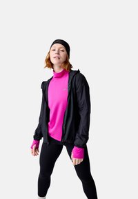 Veste légère noire sur un haut à manches longues rose vif, associée à des leggings noirs et un bandeau noir. Matière extensible pour vêtements de sport.