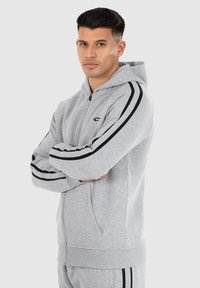 Grijze zip-up hoodie van zacht materiaal, met zwarte zijstrepen, een voorkantzak en ribgebreide manchetten en onderrand.