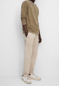 Olivgrünes Langarmshirt mit Rundhalsausschnitt, beige Chinos und weiße Sneaker mit grauen Akzenten. Glatter Stoff, lockere Passform und Seitentaschen.