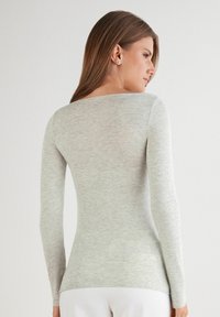 Lichtgrijs langemouwen T-shirt gemaakt van zacht, textuurstof. Heeft een bescheiden ronde halslijn en een slim fit ontwerp.