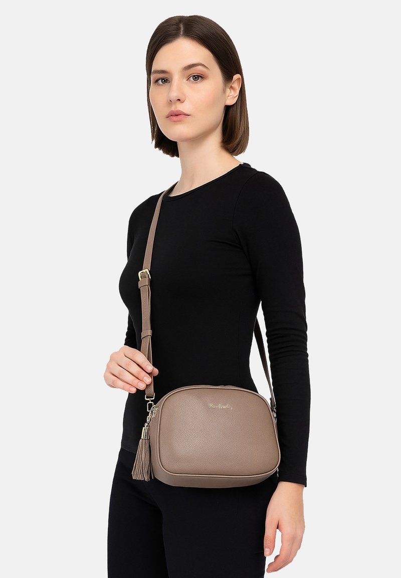 Borsa a tracolla color tan con superficie testurizzata, un accento in logo dorato e dettaglio con frange. Presenta una tracolla regolabile e una forma arrotondata.