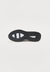 Black textured rubber shoe sole with traction grooves and white accents. Curved shape, wider midsection, and pronounced heel area.