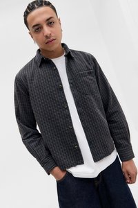 Rutete skjorte i mørke farger, med knapper foran og en brystlomme; lagdelt over en enkel hvit t-skjorte, kombinert med mørk denim jeans.