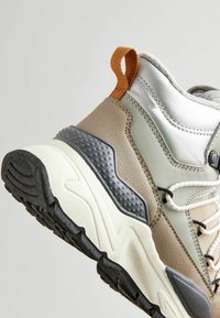 Chunky Sneaker mit einer Mischung aus beige, grau und metallischen Materialien, mit strukturierten Akzenten, weißer Zwischensohle und schwarzem Gummiaußensohle.