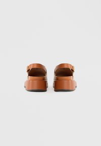 Bruine platte sandalen met enkelbandjes, met een geweven structuur en een verstelbare gesp. Effen rubberen zool voor grip.