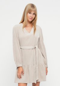 Bežna obleka z V-izrezom, dolgimi napihnjenimi rokavi, zavezanjem in širšim krilom. Narejena iz mehkega, teksturiranega blaga z diskretno sijajem.