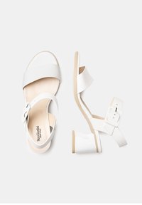 White sandals featuring smooth leather straps, a buckle accent, and a low, sculpted heel with a beige sole.