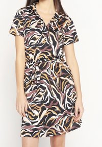 Šaty s krátkým rukávem s černým pozadím a vícebarevným abstraktním vlnitým vzorem v béžové, hnědé a bílé barvě; zavazují se v pase.
