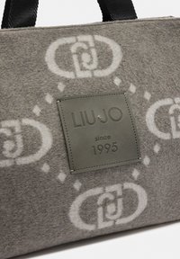 Borsa grigia in feltro con manici neri, motivo a catena bianca intrecciata, e una toppa in pelle cucita con la scritta "LIU·JO dal 1995" sul frontale.