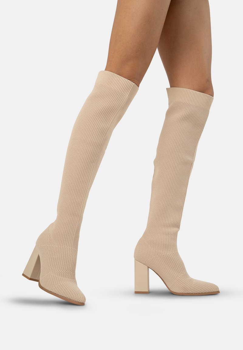 Botas de punto beige hasta la rodilla con un tacón bloque, que presentan un patrón texturizado y un diseño ajustado. Diseñadas para un ajuste ceñido alrededor de la pierna.
