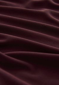 Bourgognefarvet stof draperer i bløde folder, der viser en glat tekstur og let glans med subtile variationer i bølgemønstre.