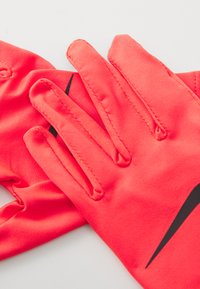 Gants de sport corail vif en tissu extensible. Présentent un logo noir distinct et des coutures, avec une couverture individuelle des doigts et une texture lisse.