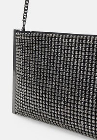 Černá kabelka na řetězovém popruhu, pokrytá stříbrnými kamínky uspořádanými do mřížkového vzoru, s elegantním obdélníkovým designem.