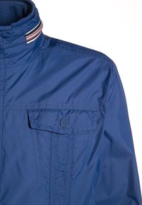 Modrá bunda s vysokým límcem, která má pruhovaný lem, kapsu s klopou a patentním knoflíkem na prsou a viditelné šití.