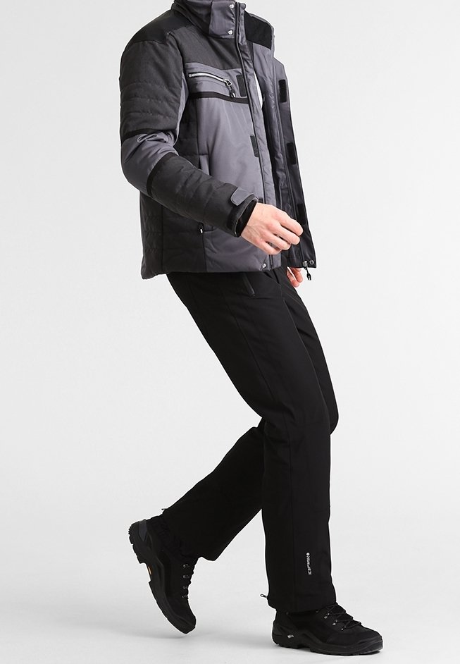 Harmaa ja musta eristetty takki vetskarillisten taskujen kanssa, yhdistettynä mustiin housuihin ja mustiin vaelluskengiin. Takissa on korkea kaulus ja teksturoidut hihansuut.