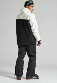 Chaqueta de nieve en blanco y negro con capucha, combinada con pantalones de esquí negros. Incluye un corte relajado y botas de esquí con marca.