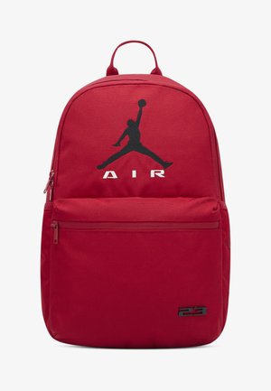Κόκκινο υφασμάτινο σακίδιο με έντονο μαύρο λογότυπο Jumpman, λευκό κείμενο «AIR» και τσέπη με φερμουάρ στο μπροστινό μέρος. Διαθέτει επάνω χερούλι και ρυθμιζόμενους ιμάντες.