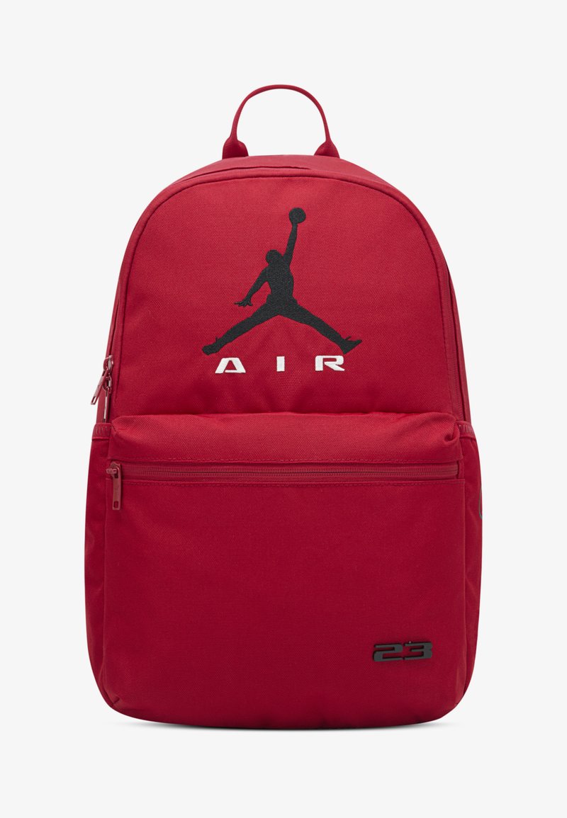 Κόκκινο υφασμάτινο σακίδιο με έντονο μαύρο λογότυπο Jumpman, λευκό κείμενο «AIR» και τσέπη με φερμουάρ στο μπροστινό μέρος. Διαθέτει επάνω χερούλι και ρυθμιζόμενους ιμάντες.