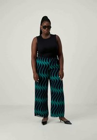 Μαύρο αμάνικο τοπ σε συνδυασμό με παντελόνι φαρδύ που έχει σκούρο τιρκουάζ κυματιστό σχέδιο σε μαύρ�ο φόντο; συμπληρωμένο με μαύρα μυτερά παπούτσια.