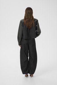 Black denim cropped jacket with leather sleeves, paired with wide-leg black denim pants and beige high heels, viewed from the back.