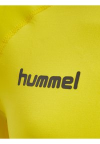 Gul atletisk skjorte med glat, strækbart stof og kontrasterende sort "hummel" logo. Forstærkede sømme øger holdbarheden af designet.